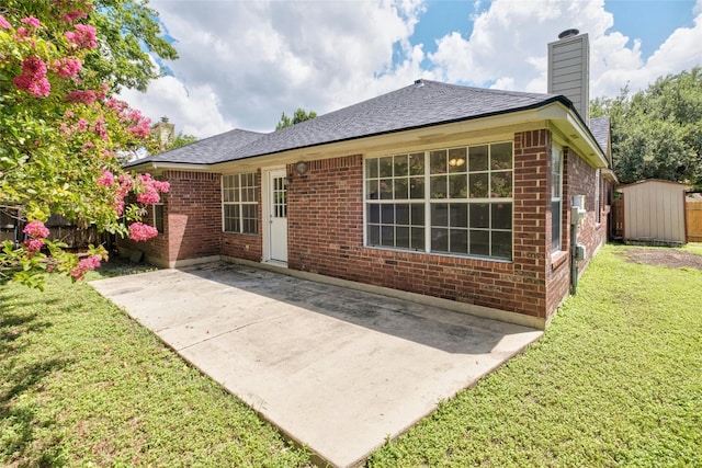 back of property with an outbuilding, brick siding, a yard, a chimney, and a patio area