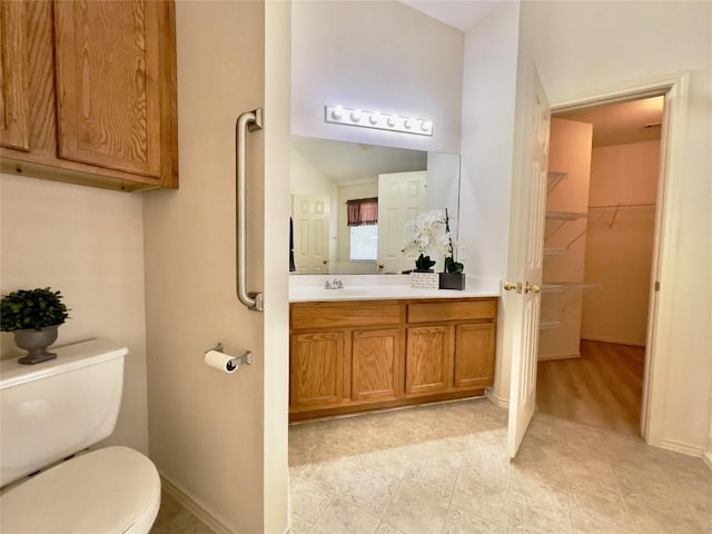 bathroom featuring a walk in closet, vanity, toilet, and baseboards