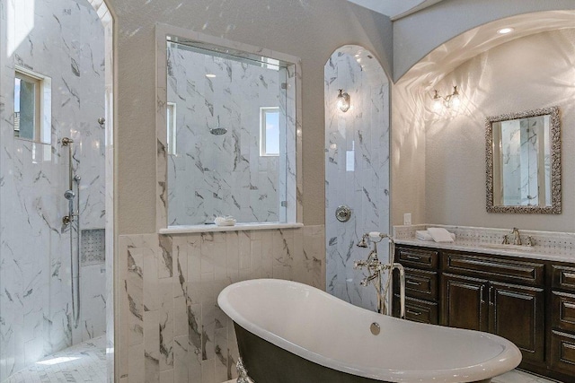 full bath featuring a marble finish shower, tile walls, a freestanding bath, and vanity