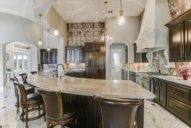 kitchen with arched walkways, a sink, high quality appliances, marble finish floor, and custom exhaust hood