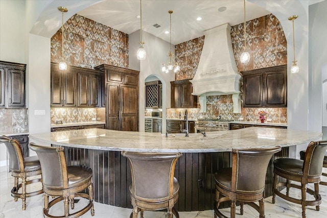 kitchen with premium range hood, light stone counters, backsplash, and a sink