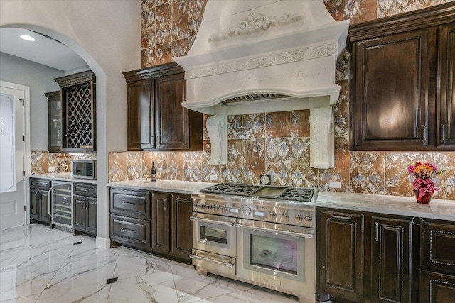 kitchen with marble finish floor, custom exhaust hood, range with two ovens, and decorative backsplash