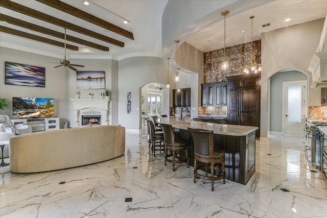 kitchen featuring arched walkways, a warm lit fireplace, a breakfast bar area, high quality appliances, and light stone countertops