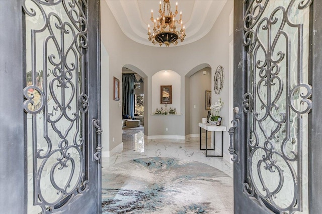 foyer with arched walkways, baseboards, marble finish floor, a tray ceiling, and an inviting chandelier