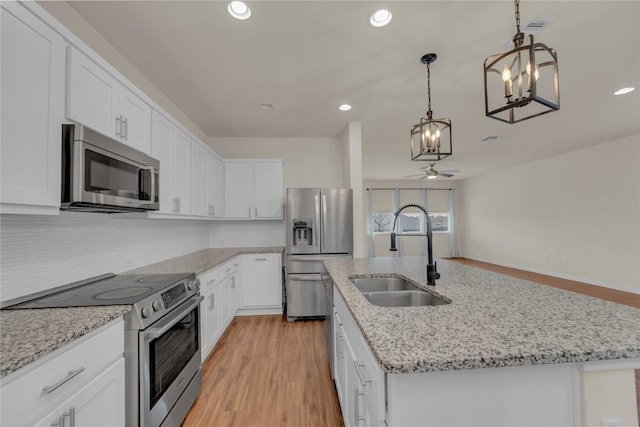 kitchen with stainless steel appliances, an island with sink, a sink, and white cabinetry