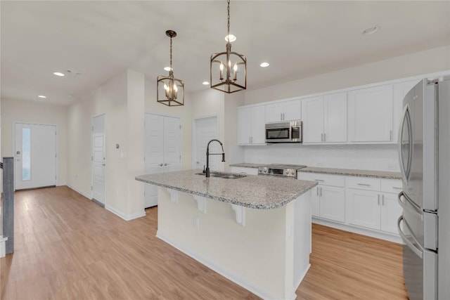 kitchen featuring light wood-style flooring, stainless steel appliances, a sink, white cabinetry, and a center island with sink