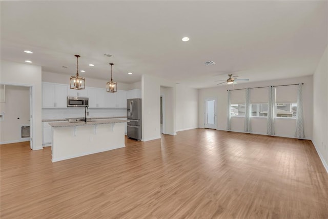 kitchen with ceiling fan, stainless steel appliances, white cabinetry, open floor plan, and a center island with sink