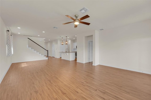 unfurnished living room featuring visible vents, a ceiling fan, stairway, light wood-style floors, and recessed lighting