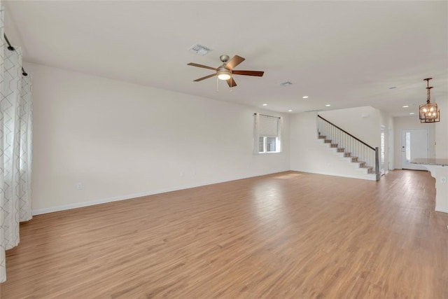 unfurnished room featuring baseboards, visible vents, stairs, light wood-style floors, and ceiling fan with notable chandelier