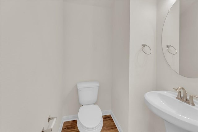 half bath with toilet, a sink, baseboards, and wood finished floors