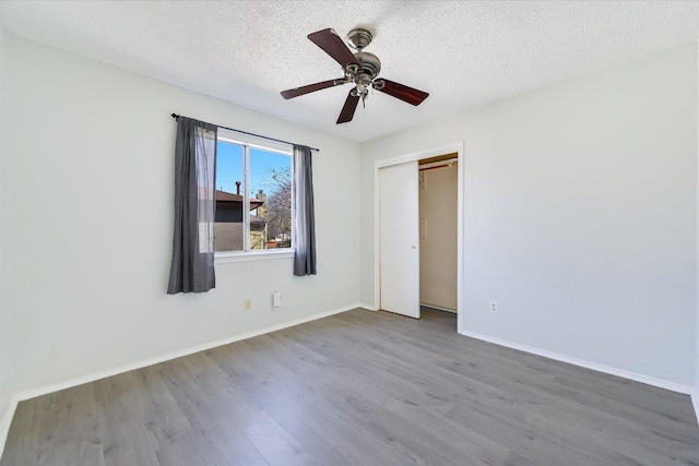 unfurnished bedroom featuring baseboards, ceiling fan, wood finished floors, a textured ceiling, and a closet