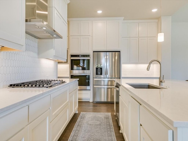 kitchen with stainless steel appliances, a sink, white cabinets, wall chimney range hood, and backsplash