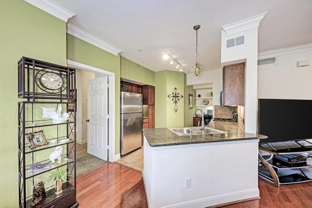 kitchen with visible vents, ornamental molding, freestanding refrigerator, a peninsula, and a sink