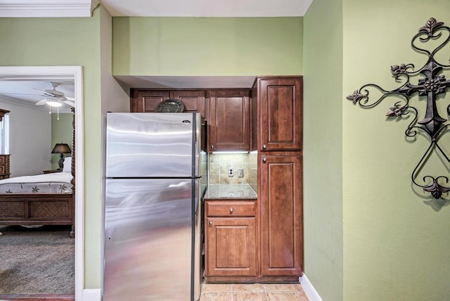 kitchen featuring stone counters, crown molding, backsplash, freestanding refrigerator, and baseboards