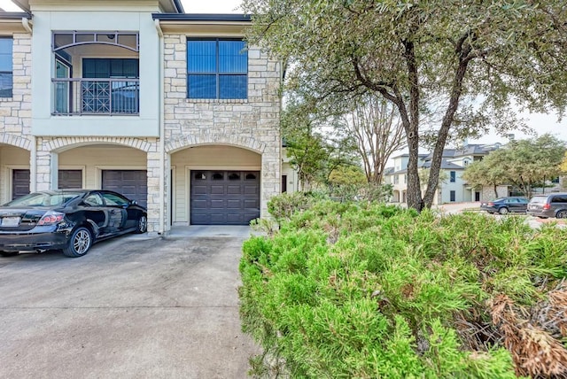 multi unit property featuring stone siding, driveway, and an attached garage