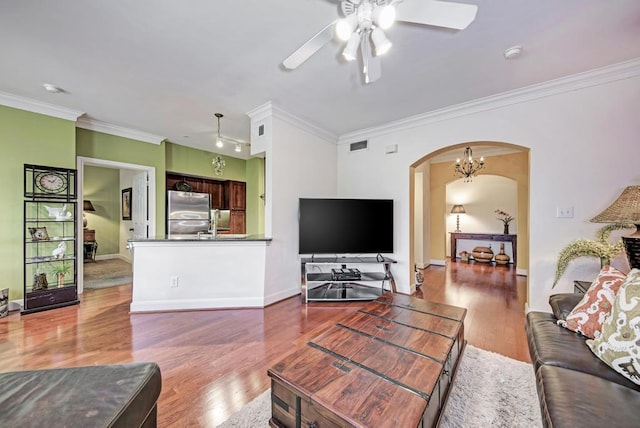 living area featuring baseboards, visible vents, arched walkways, wood finished floors, and crown molding