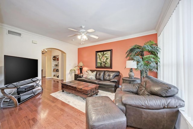 living area with arched walkways, crown molding, visible vents, a ceiling fan, and wood finished floors