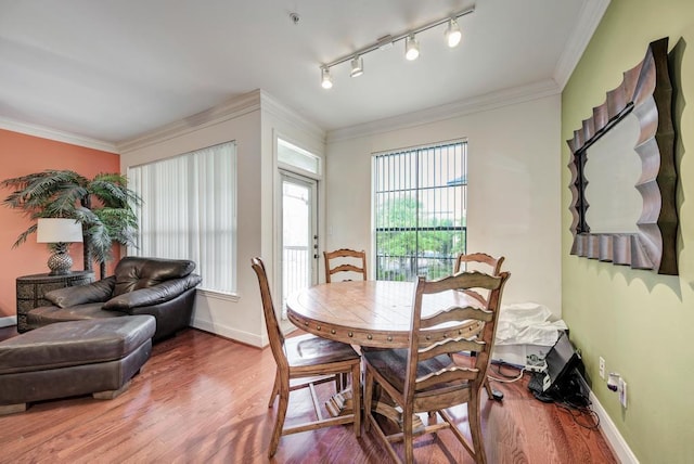 dining area featuring ornamental molding, wood finished floors, rail lighting, and baseboards