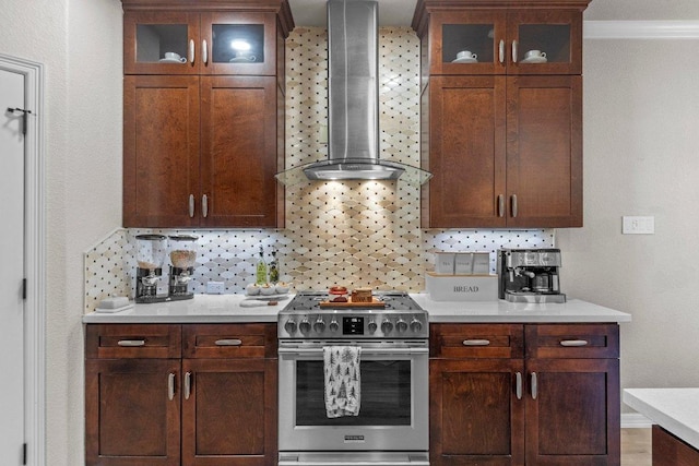 kitchen featuring wall chimney exhaust hood, stainless steel gas range oven, tasteful backsplash, and light countertops