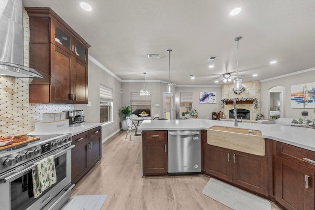 kitchen featuring wall chimney exhaust hood, appliances with stainless steel finishes, light countertops, crown molding, and a fireplace