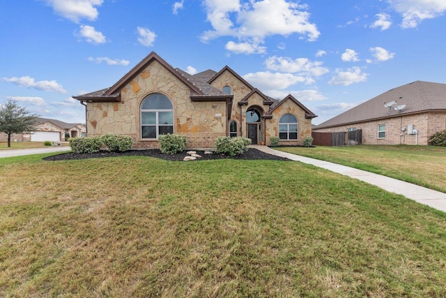 french provincial home with stone siding, fence, and a front yard