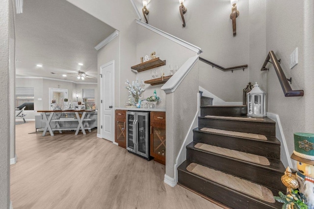 stairs featuring wine cooler, a dry bar, ornamental molding, wood finished floors, and baseboards