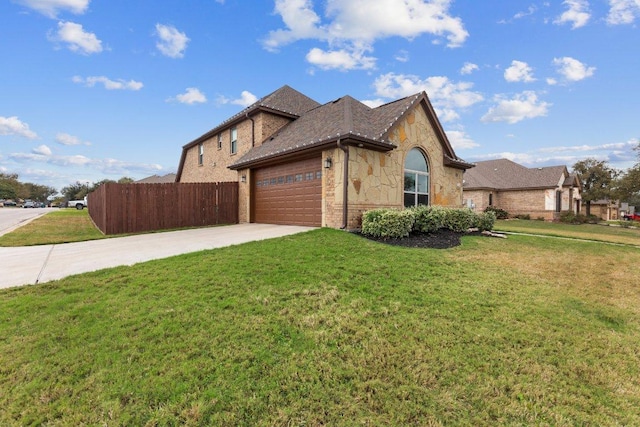 view of side of property with driveway, a garage, stone siding, fence, and a yard