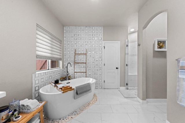 bathroom with marble finish floor, tiled shower, a freestanding bath, and baseboards