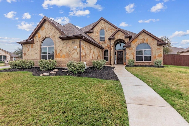 french country home featuring a shingled roof, fence, and a front yard