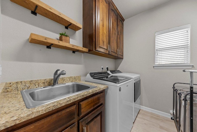 clothes washing area featuring cabinet space, light wood-style flooring, a sink, independent washer and dryer, and baseboards