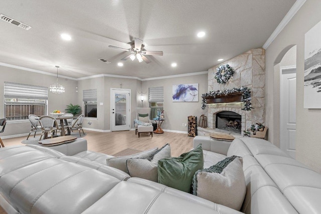 living room featuring ceiling fan with notable chandelier, a fireplace, wood finished floors, visible vents, and ornamental molding