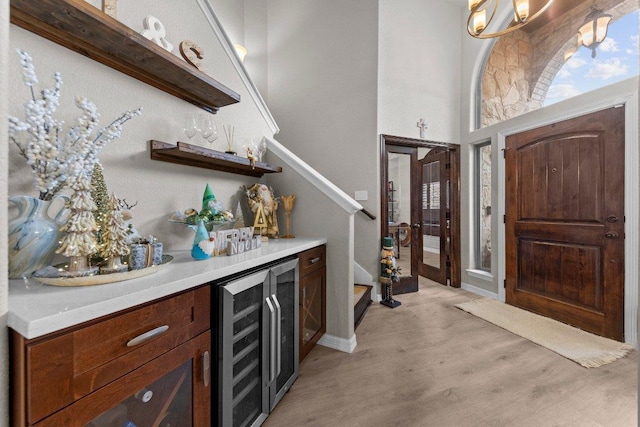 entryway featuring beverage cooler, a towering ceiling, stairs, a bar, and light wood-style floors