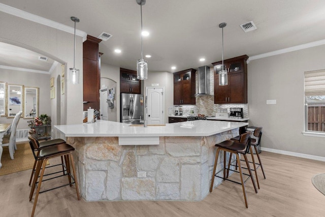 kitchen featuring visible vents, arched walkways, stainless steel fridge with ice dispenser, wall chimney exhaust hood, and crown molding