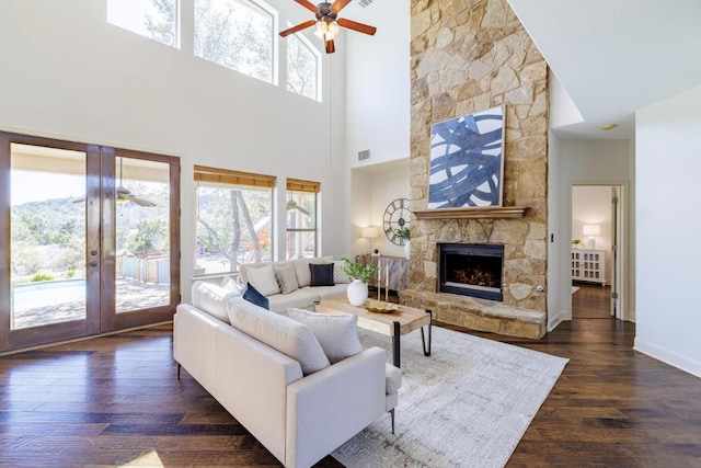 living area featuring french doors, dark wood finished floors, a wealth of natural light, and a stone fireplace