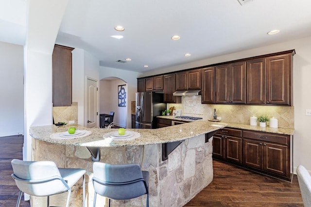 kitchen featuring dark wood-style floors, arched walkways, light stone counters, stainless steel fridge with ice dispenser, and a kitchen breakfast bar