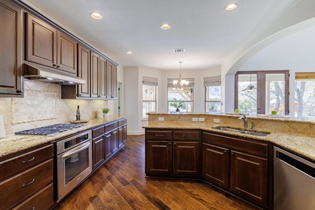 kitchen with light stone counters, dark wood-type flooring, stainless steel appliances, under cabinet range hood, and a sink