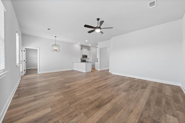 unfurnished living room featuring light wood-style floors, visible vents, baseboards, and ceiling fan with notable chandelier