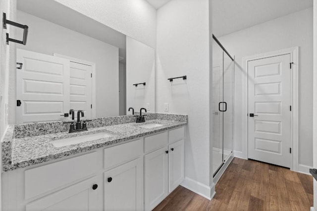 bathroom with double vanity, wood finished floors, a stall shower, and a sink