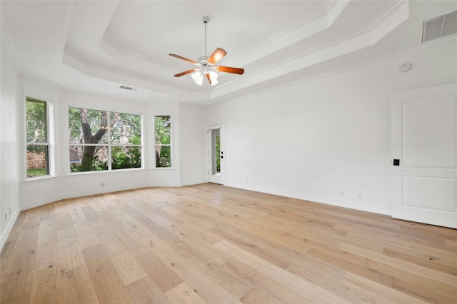 spare room with ornamental molding, a raised ceiling, visible vents, and light wood-style floors