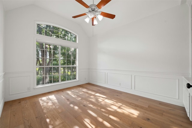 spare room featuring lofted ceiling, ceiling fan, light wood finished floors, and a wainscoted wall