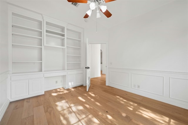 interior space featuring built in shelves, light wood finished floors, visible vents, wainscoting, and ceiling fan