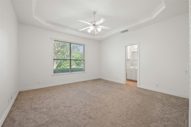 spare room with a raised ceiling, light colored carpet, visible vents, a ceiling fan, and baseboards