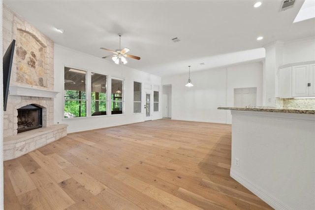 unfurnished living room with a stone fireplace, light wood-type flooring, visible vents, and a ceiling fan