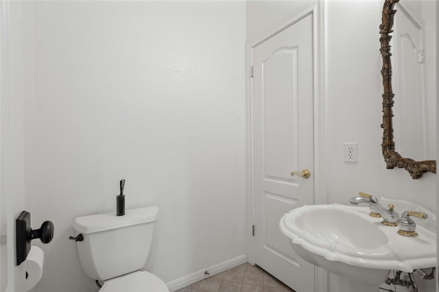 half bathroom with toilet, baseboards, a sink, and tile patterned floors