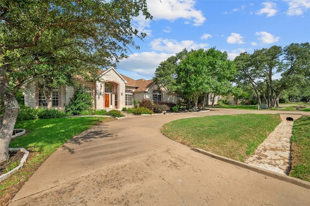 view of front of house with stone siding, concrete driveway, and a front yard