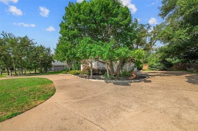 exterior space with concrete driveway, fence, and a front lawn