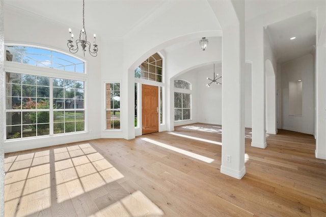 entrance foyer featuring arched walkways, light wood-style flooring, a notable chandelier, baseboards, and crown molding