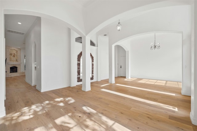 spare room featuring a chandelier, wood-type flooring, visible vents, and a fireplace