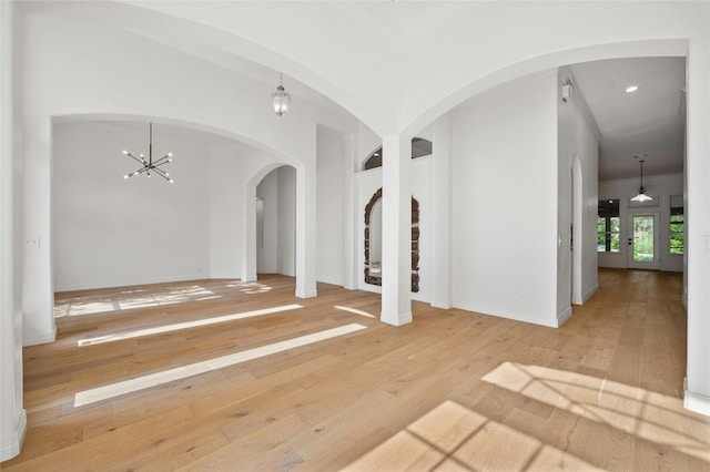 empty room featuring arched walkways, wood-type flooring, and an inviting chandelier