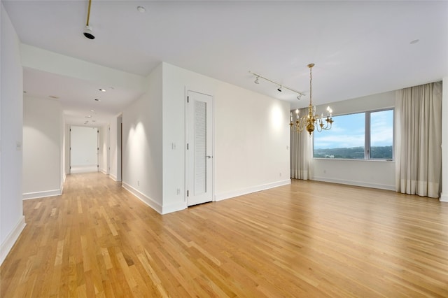 spare room featuring light wood-style floors, baseboards, a chandelier, and track lighting